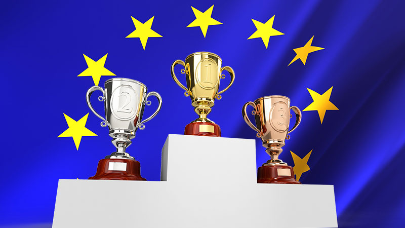 Trofées posés sur les marches d'un podium sur fond de drapeau européen