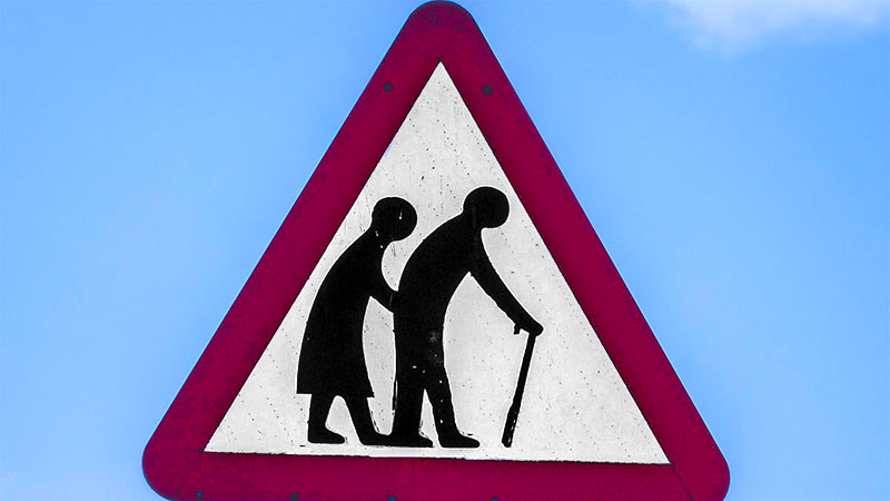 Panneau de signalisation triangulaire figurant deux silhouettes courbées se tenant sur une canne. © K. Mitch Hodge on Unsplash