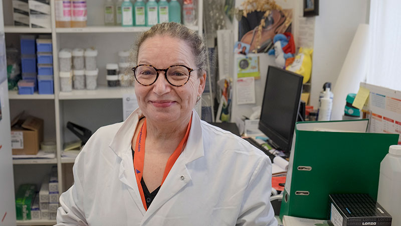 Femme souriante vêtue d'une blouse dans un bureau encombré.
