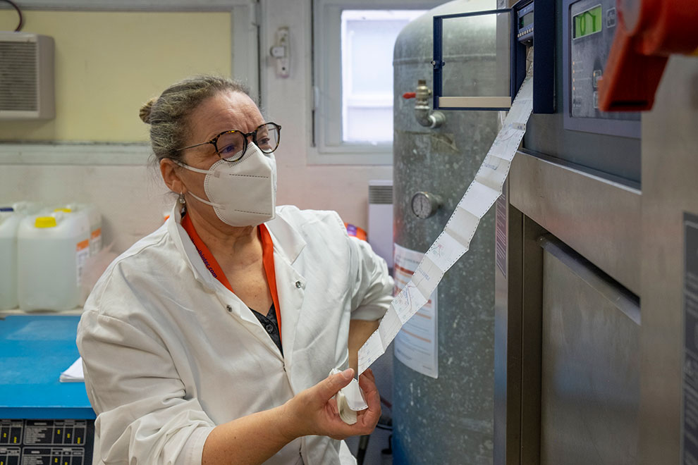 Femme vêtue d'une blouse et d'un masque consultant un rouleau de papier produit par l'autoclave.